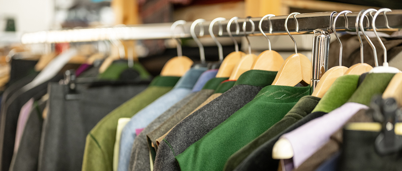 Kleiderstange mit vielen Lodenjacken in verschiedenen Grau- und Grüntönen.